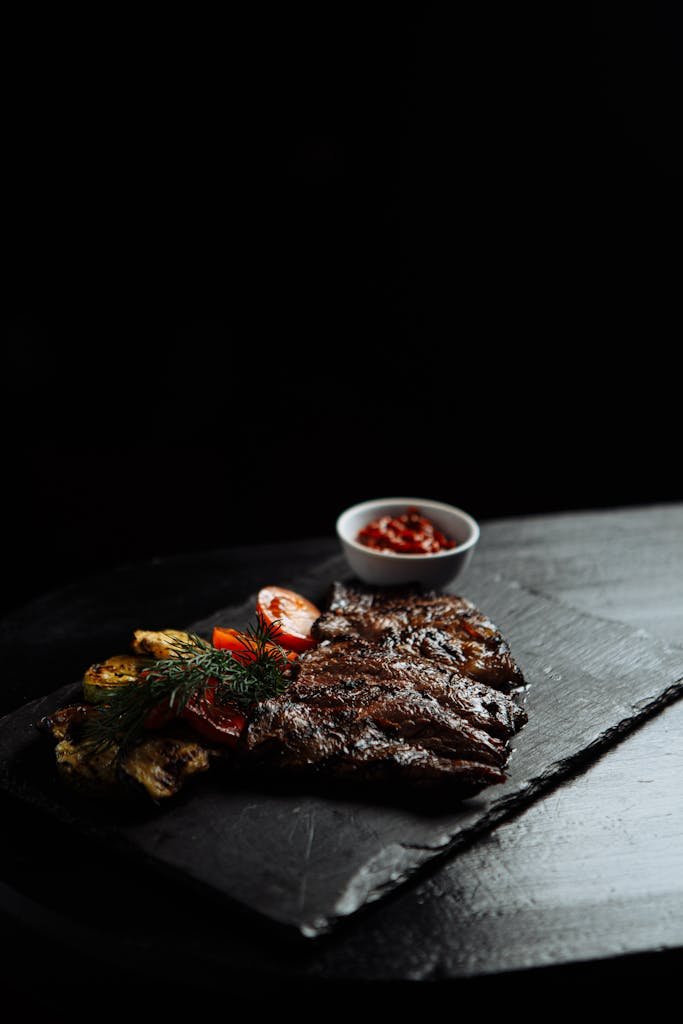 Appetizing grilled steak served with vegetables and sauce on a sleek slate board.